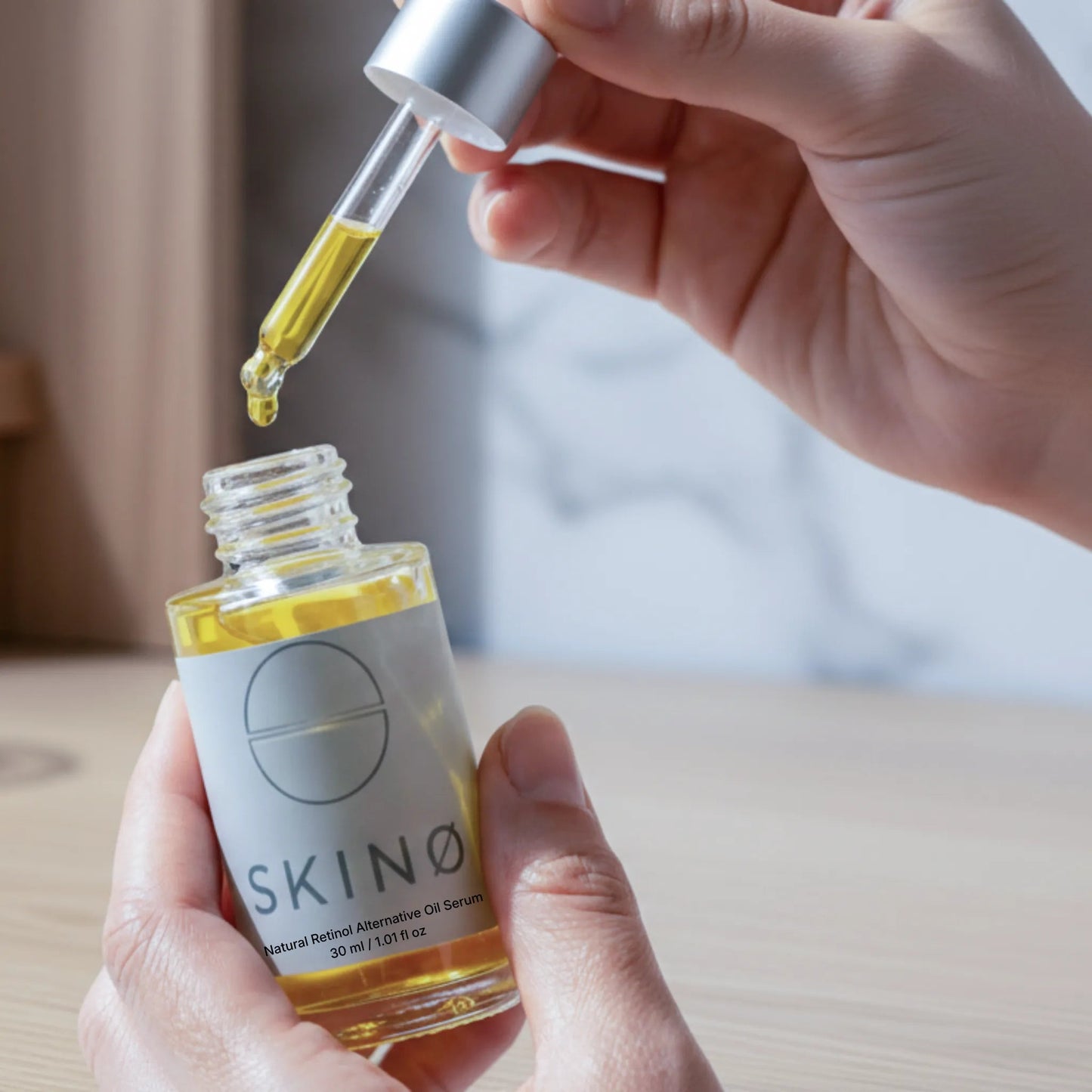 Hand håller SKINØ Natural Retinol Alternative Oil Serum 30ml – dropper med gyllene bakuchiololja, naturligt retinolalternativ för fasthet och förnyelse av huden.