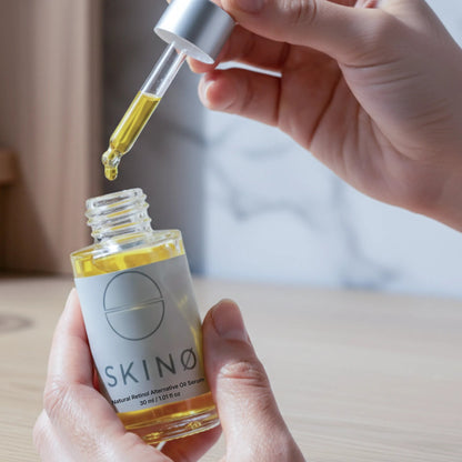 Hand håller SKINØ Natural Retinol Alternative Oil Serum 30ml – dropper med gyllene bakuchiololja, naturligt retinolalternativ för fasthet och förnyelse av huden.