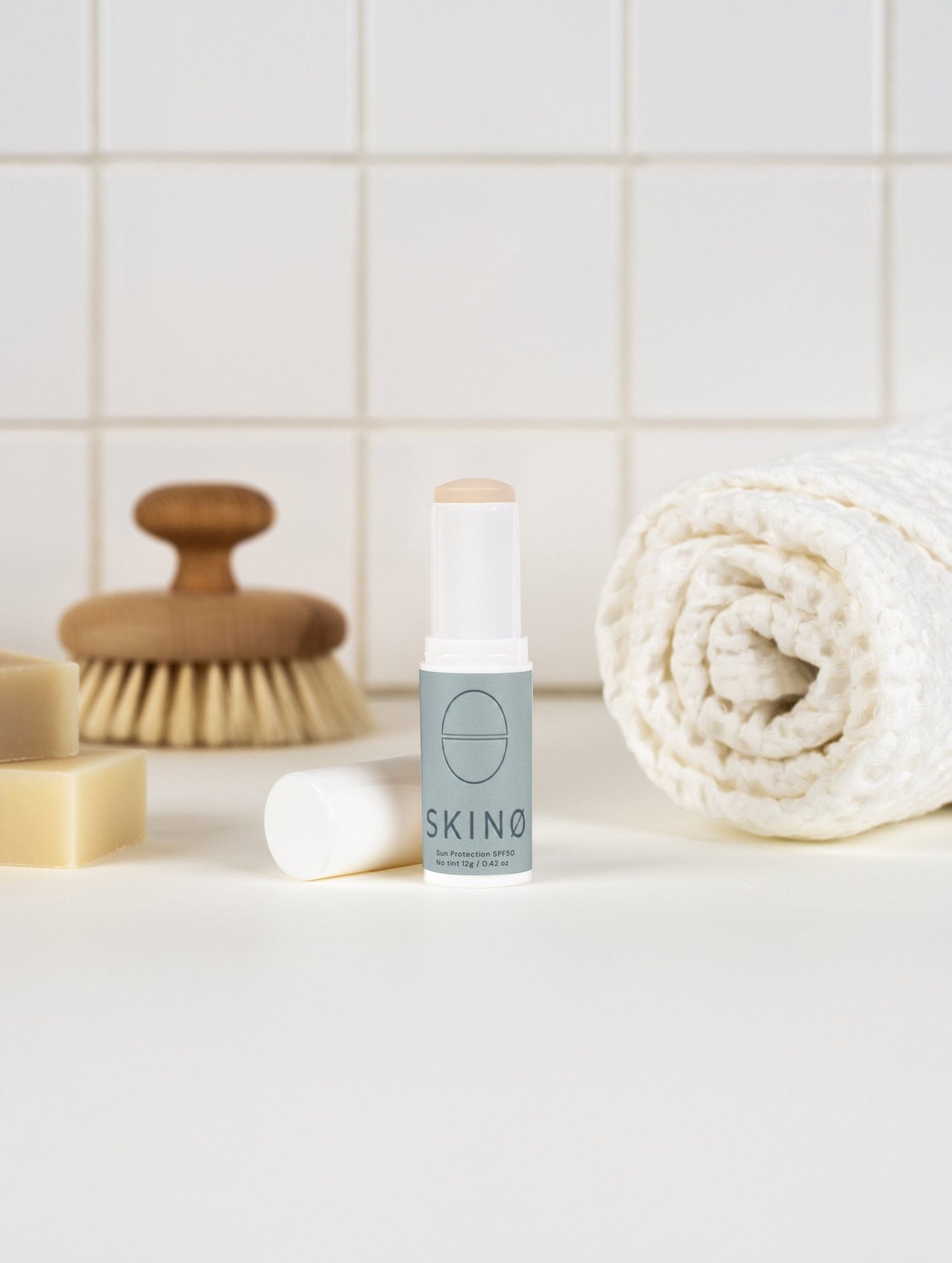 SKINØ Mineral Sun Stick SPF 50 lifestyle – mineral solskyddsstick 
placerad i spa-inspirerad badrumsscen med naturliga badtillbehör, 
representerar daglig hudvård rutiner med ekologisk, reef-safe 
sunscreen för känslig och mogen hud, COSMOS ORGANIC certifierad 
naturlig skincare.